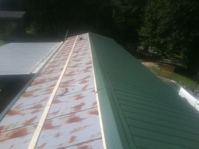 Old rusted panels beside newly installed green metal roofing — Wind Damage Roof Repair by Roofing Brothers in Braddock